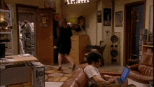 a man is sitting on a couch using a laptop while a woman walks by