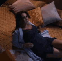 a woman in a black dress is laying on a bed with pillows