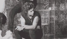 a black and white photo of a man sitting on the floor with his arms crossed .