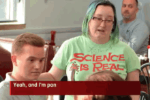 a woman wearing a green shirt that says science is real talks to a man