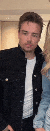 a man in a black denim jacket and a white shirt is standing next to a woman .