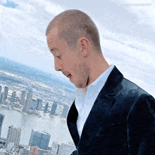 a man in a suit stands in front of a city skyline with the words josephquinngifs below him
