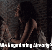 a woman sitting in front of a brick wall with the words " we negotiating already "