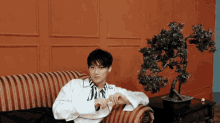 a man in a white shirt is sitting on a couch next to a potted plant