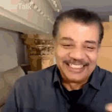 a man with a mustache is smiling while wearing a blue shirt and a black shirt .