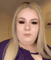 a woman with blonde hair is wearing a purple top and a necklace