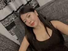 a woman in a black tank top sits on a couch in front of a curtain