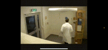 a man in a lab coat is walking down a hallway with a ladder in the background .