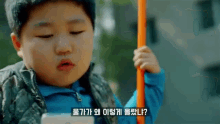 a young boy in a blue jacket is holding an orange stick and a cell phone in his hand .