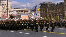 a group of soldiers march down a street in front of a building with the number 00 on it