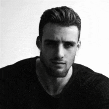 a black and white photo of a man with a beard in a black shirt .