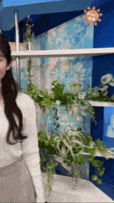 a woman is standing in front of a shelf with plants and a sign that says ' おはよう '