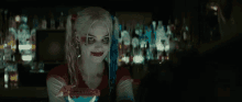 a woman in a harley quinn costume is smiling while holding a drink in a bar .