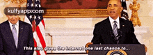 a man in a suit and tie is giving a speech in front of two american flags .