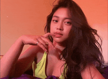a woman wearing a yellow tank top and a ring on her finger looks at the camera