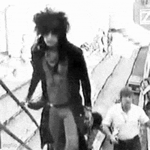 a black and white photo of a man walking down stairs with a man standing behind him .