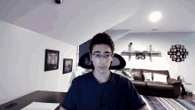 a young man wearing glasses sits in front of a couch in a living room