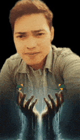 a man in a denim shirt holds his hands up in front of a picture of a waterfall behind him