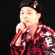 a man wearing a black hat and a red shirt with the word gdl on the sleeve is singing into a red microphone