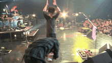 a man in a plaid shirt stands on a stage with his hands in the air