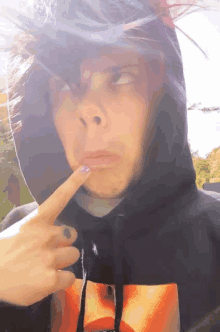 a person wearing a black hoodie has their finger on their chin