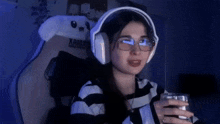 a woman wearing headphones and glasses is sitting in a chair and holding a glass of water .