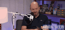 a man sitting in front of a microphone with dark web written on the bottom right