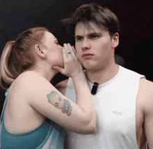 a woman whispering into a man 's ear with a tattoo of a cartoon character on her arm