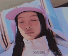 a woman wearing a pink hat and a white jacket is laying on a striped blanket