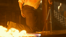 a man kneeling down holding a sword in front of flames
