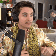 a man wearing headphones and a scarf stands in front of a microphone with a leopard print shirt on