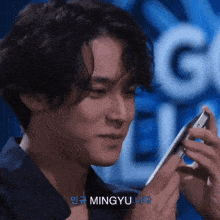 a young man is holding a cell phone in front of a sign that says ' mingyu ' on it