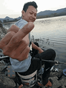 a man is giving the middle finger while sitting by the water