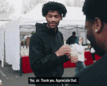 a man in a black hoodie is talking to another man and says " yes sir thank you appreciate that "