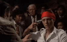a man with a red headband is holding a gun to his head