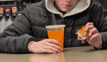 a person sitting at a table drinking orange juice and eating a burger
