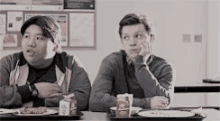 two young men are sitting at a table with a tray of food in a cafeteria .