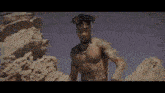 a shirtless man is standing on top of a rocky hill in the desert .