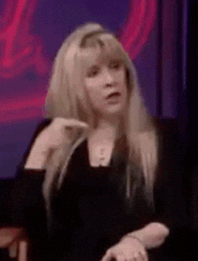 a woman with long blonde hair is sitting in front of a red background and making a funny face .