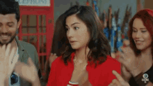 a woman in a red shirt stands in front of a red telephone booth and a group of people clapping