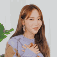 a close up of a woman wearing a sweater and earrings with her hands on her chest .