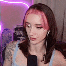 a woman with pink hair is wearing headphones and a blue tank top while talking into a microphone .