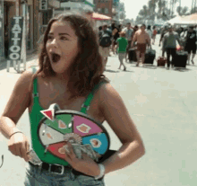 a woman in a green tank top is holding a wheel of fortune in front of her face .