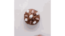 a person is holding a cookie with marshmallows and chocolate chips on top of it .