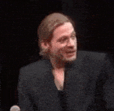 a man in a suit and ponytail is laughing and holding a glass of wine .