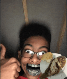 a young boy with glasses is holding a plate of food in front of his face