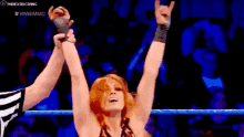a woman in a wrestling ring with her arms in the air and a referee .