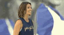 a woman in a blue tank top is smiling while standing in front of a blue and white flag .