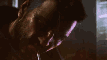 a close up of a man smoking a cigarette with a purple light behind him