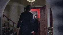 two men are standing in front of a red door with a lamp above them